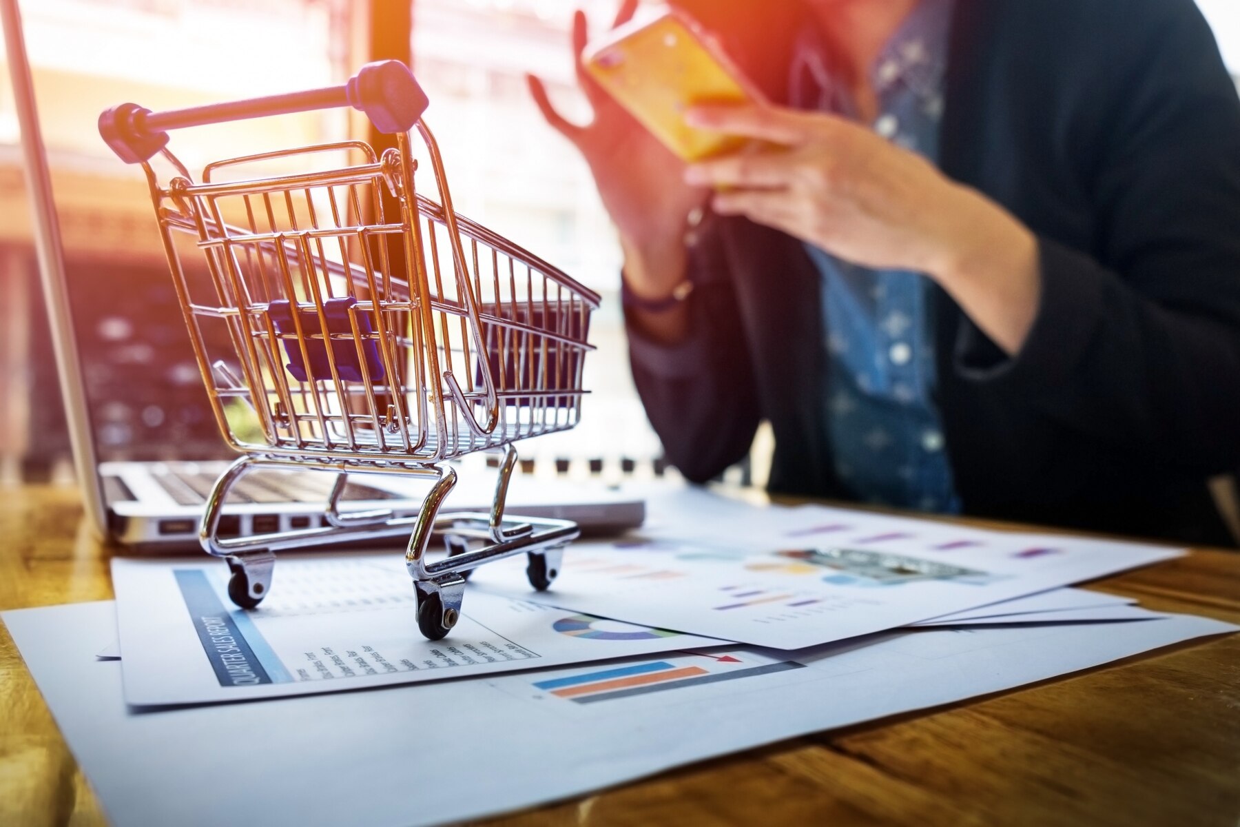 Shopping cart beside a laptop and a customer using a phone